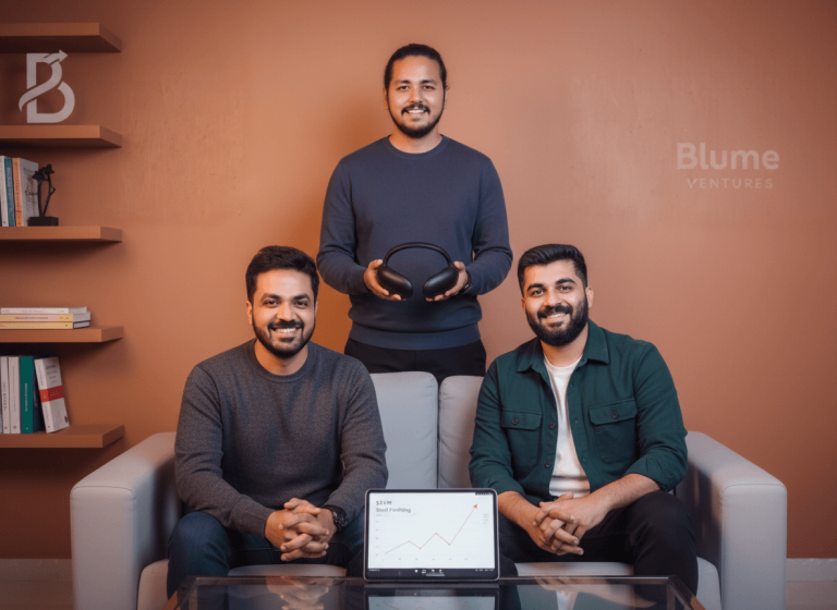 Three smiling men, two seated and one standing, displaying a wearable headset and a tablet with a graph, with "Blume Ventures" text.
