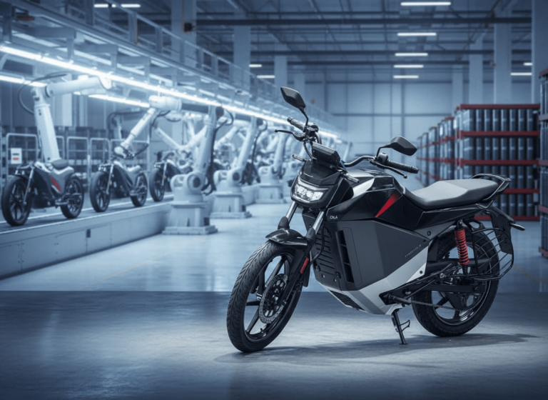 An electric motorcycle, the Ola Electric Roadster, parked in a sleek, automated factory setting with robots and other bikes.