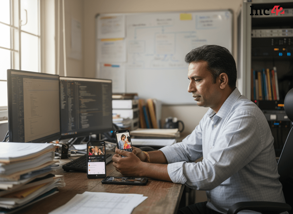A man in a collared shirt intensely watches content on a smartphone, with other phones and computer screens on a desk.